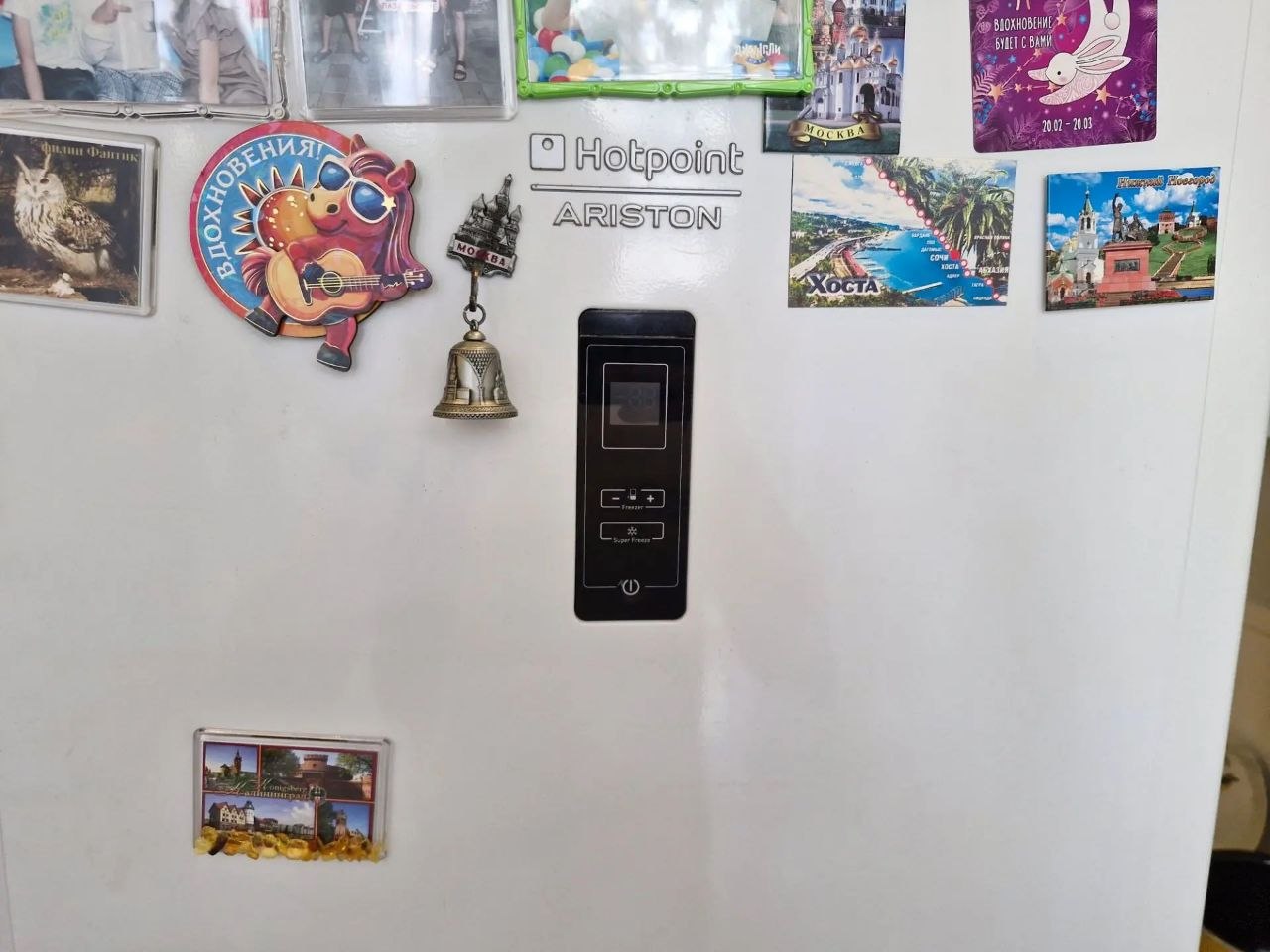 Ремонт компрессора холодильника Ariston Дверца холодильника с логотипом Hotpoint Ariston и шильдиком модели; открытая нижняя панель и область с компрессором во время ремонта